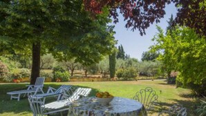Un jardín con una mesa redonda y sillas, rodeado de follaje y árboles.