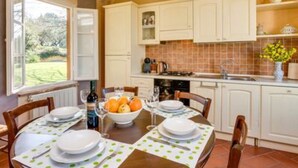 Una cocina con armarios blancos, salpicadero de azulejos y una mesa de comedor con platos y un tazón de fruta.