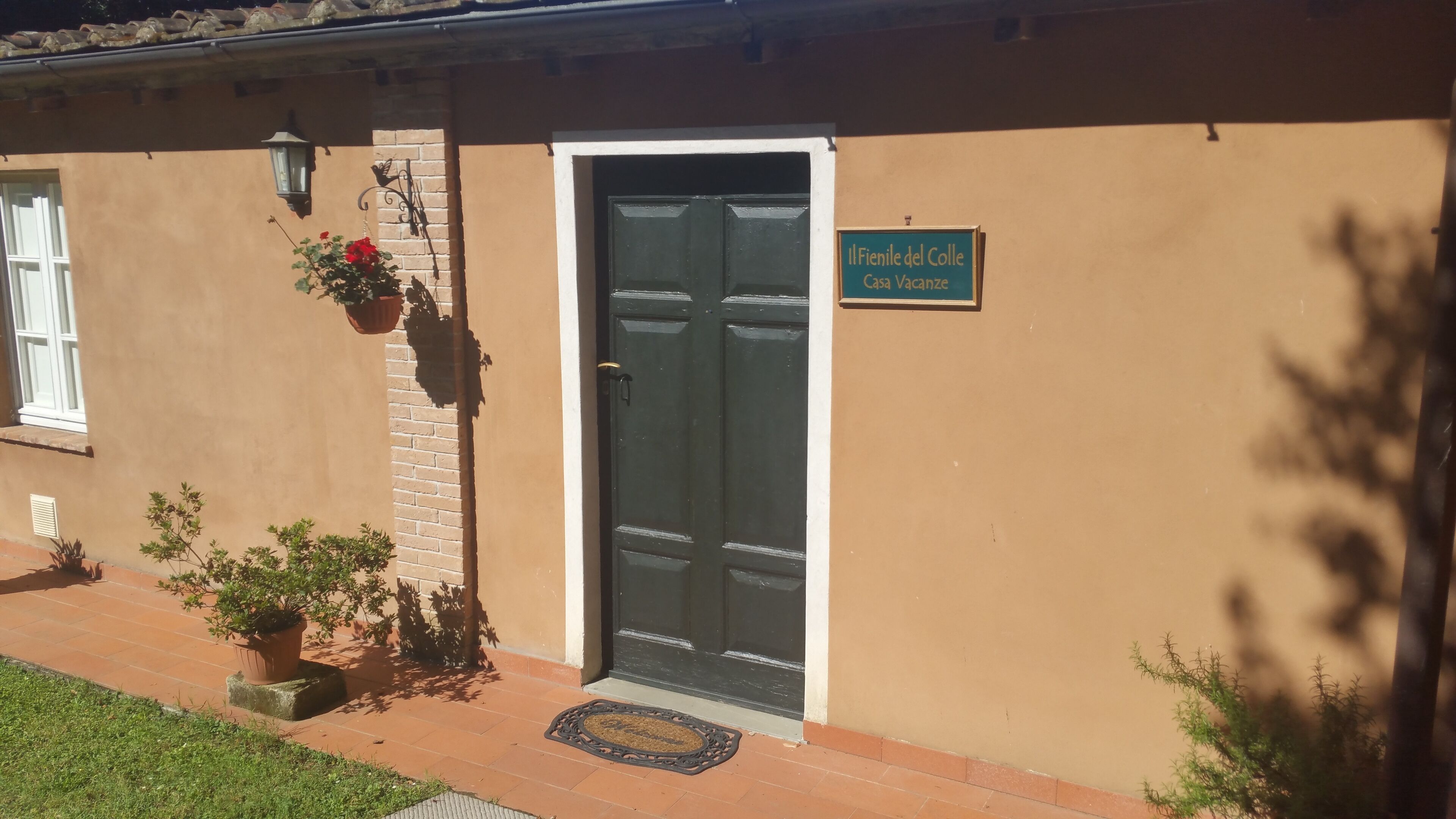 Ein Gebäude mit einer dunklen Tür, einem Schild mit der Aufschrift 'Il Fenile del Colle Casa Vacanze' und Topfpflanzen auf der Veranda.