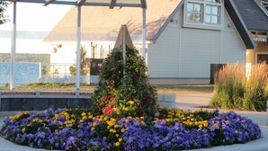 A building with a covered outdoor area, a flower bed with purple and yellow flowers, and a view of a body of water.