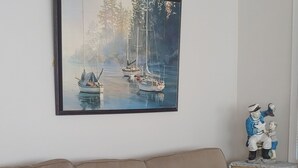 A beige sofa with a patterned pillow, a framed painting of sailboats, and a small figurine on a side table.