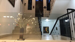 Un intérieur spacieux agrémenté d’un escalier, d’une rambarde en verre et d’œuvres d’art aux murs.