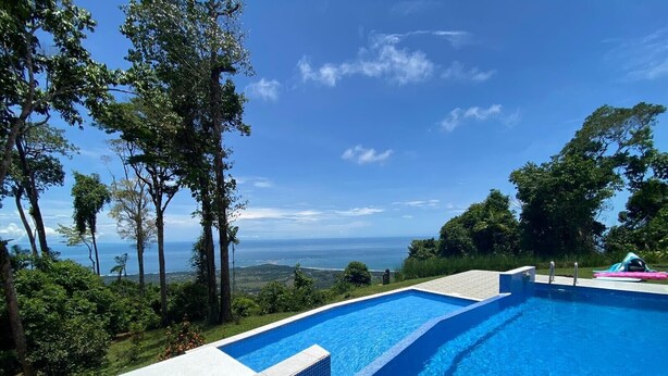 Une piscine à l’eau d’un bleu cristallin, entourée d’une végétation luxuriante et d’arbres, offrant une vue imprenable sur l’océan.