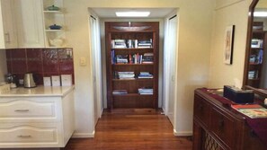 A hallway with a wooden bookshelf, a kitchen area with a coffee maker, and a dresser with a mirror.