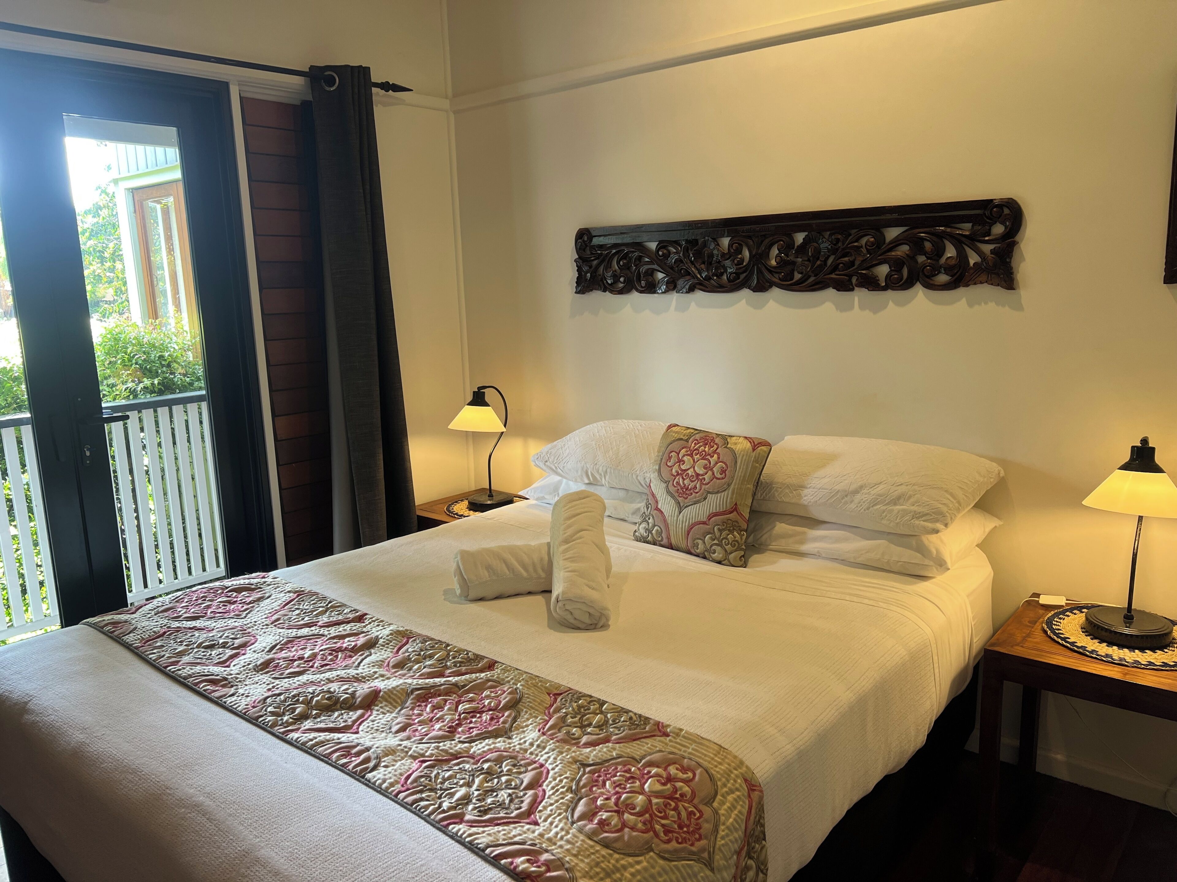 A hotel room with a bed, two bedside lamps, a decorative wall piece, and a balcony with a view.