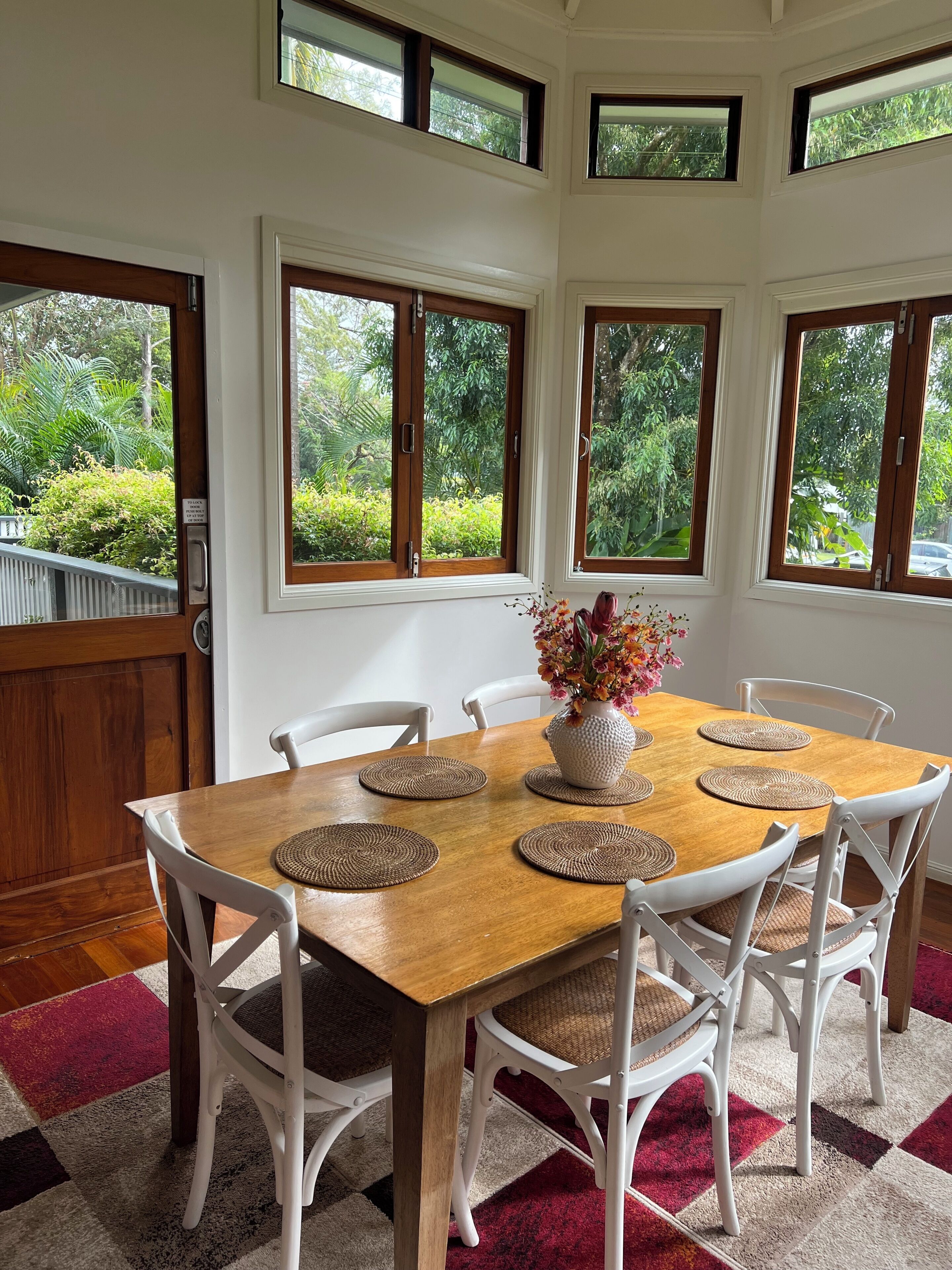 A dining area with a wooden table, white chairs, and a vase of flowers.