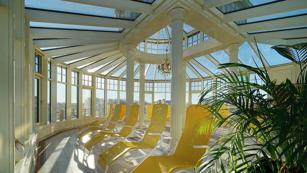 A sunroom with large windows, a chandelier, and yellow lounge chairs. - Hotel Strandperle (Cuxhaven)