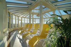 A sunroom with large windows, a chandelier, and yellow lounge chairs. - Hotel Strandperle (Cuxhaven)