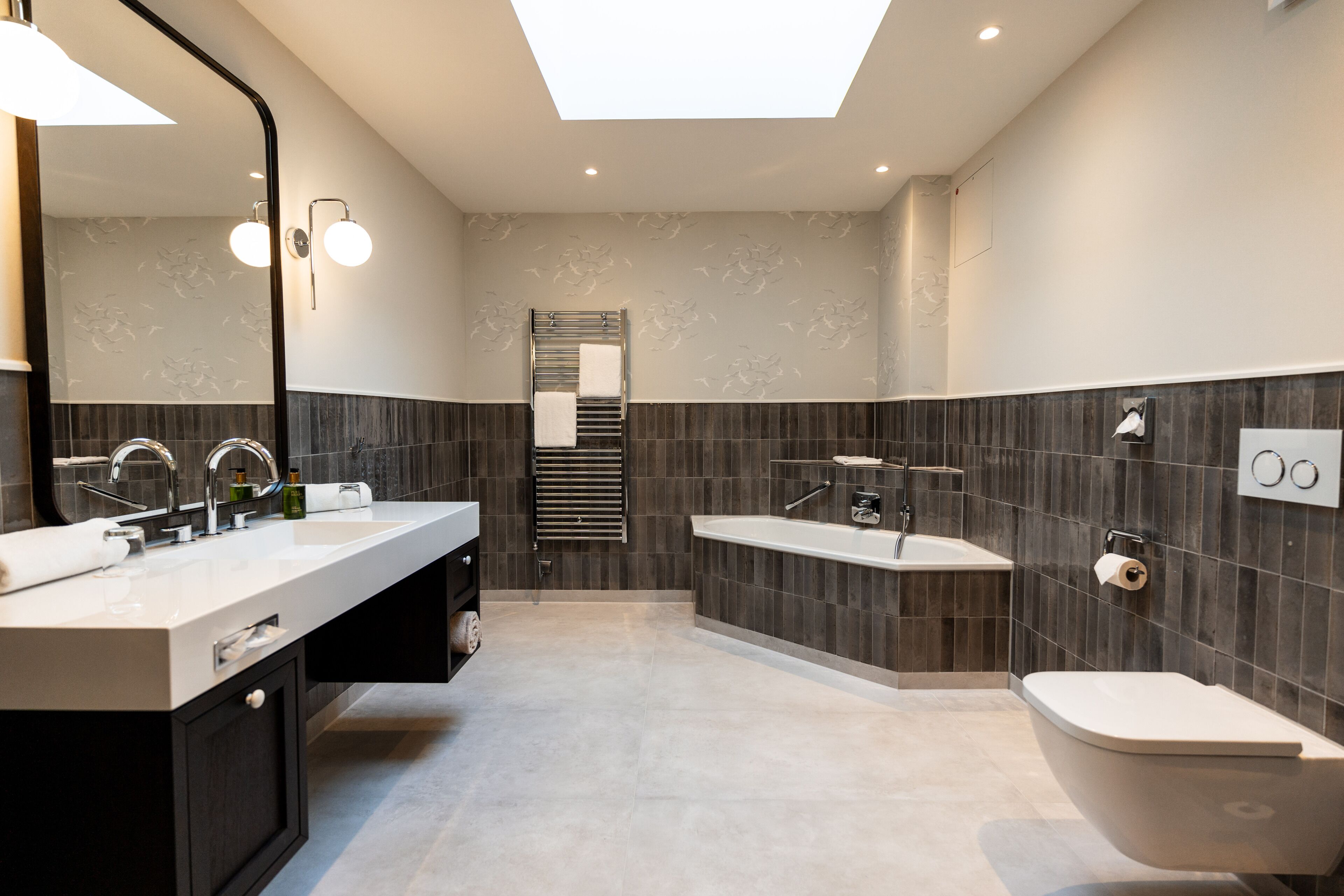 A modern bathroom with a large mirror, two sinks, a bathtub, and a toilet.
