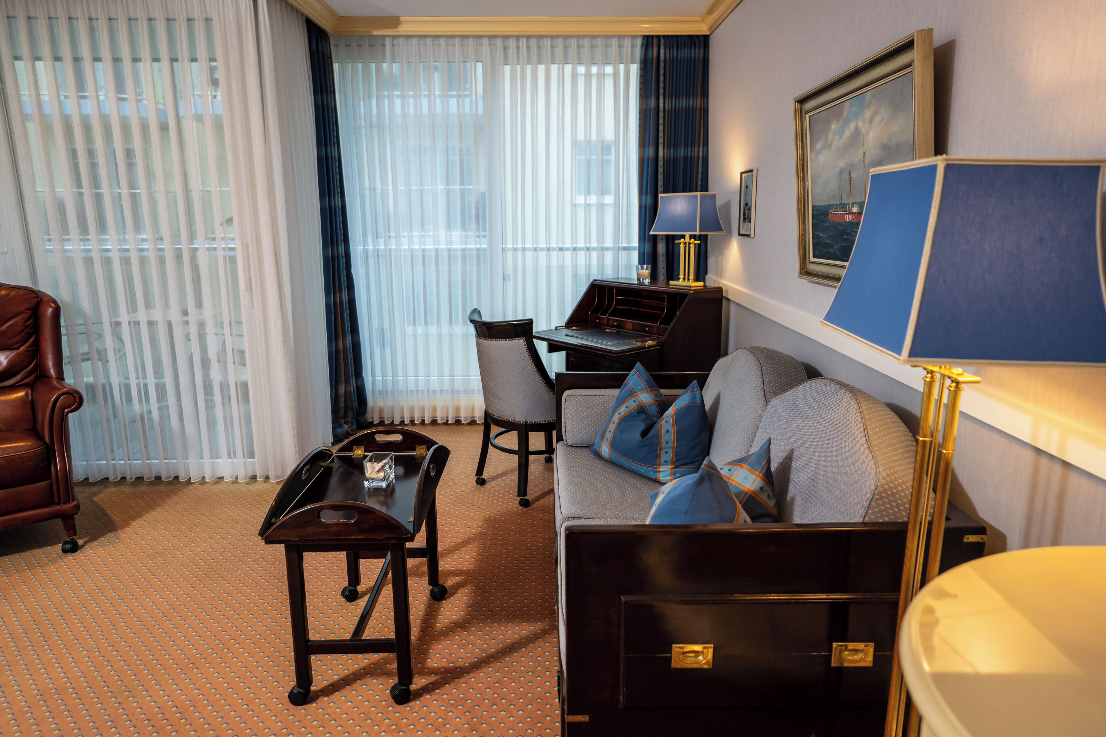 A hotel room with a sofa, armchair, desk, and a lamp.