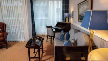 A hotel room with a sofa, armchair, desk, and a lamp.