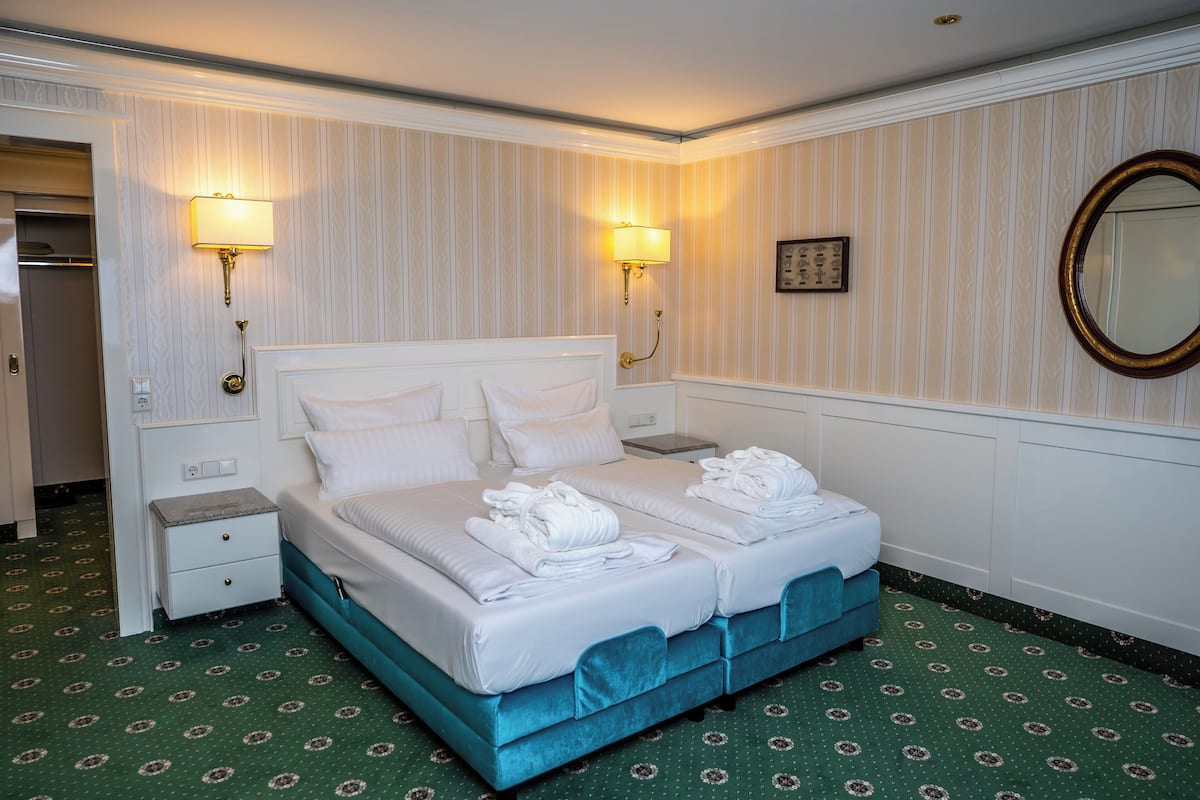 Habitación de hotel con una cama doble, dos mesitas de noche, un tocador, un espejo y una lámpara de pared.