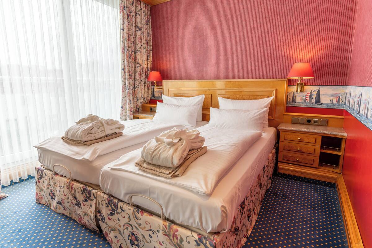 Habitación de hotel con cama doble, dos mesitas de noche, un tocador y una ventana con cortinas.