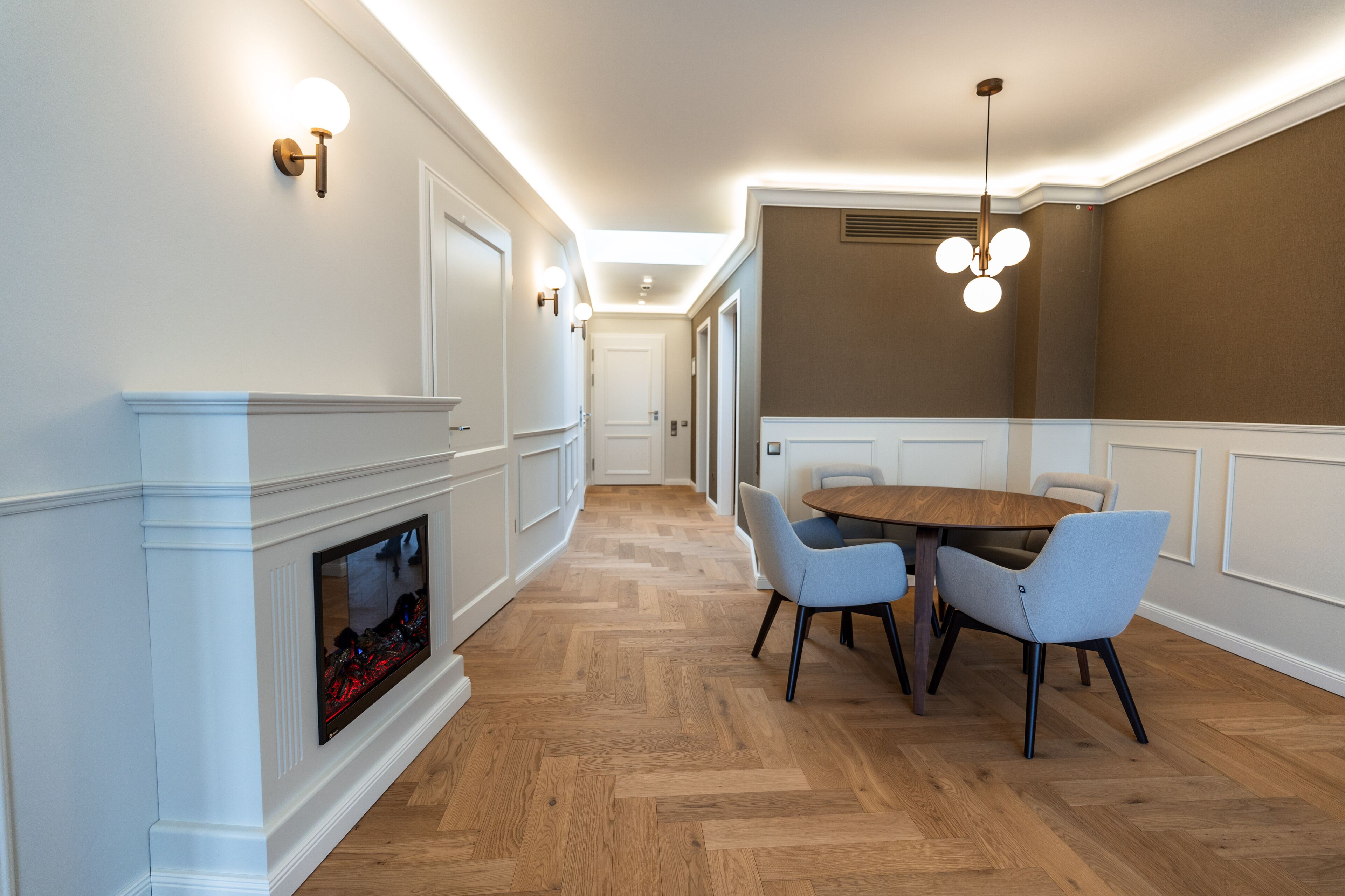 A modern dining area with a wooden herringbone floor, a round table, and two light blue chairs.