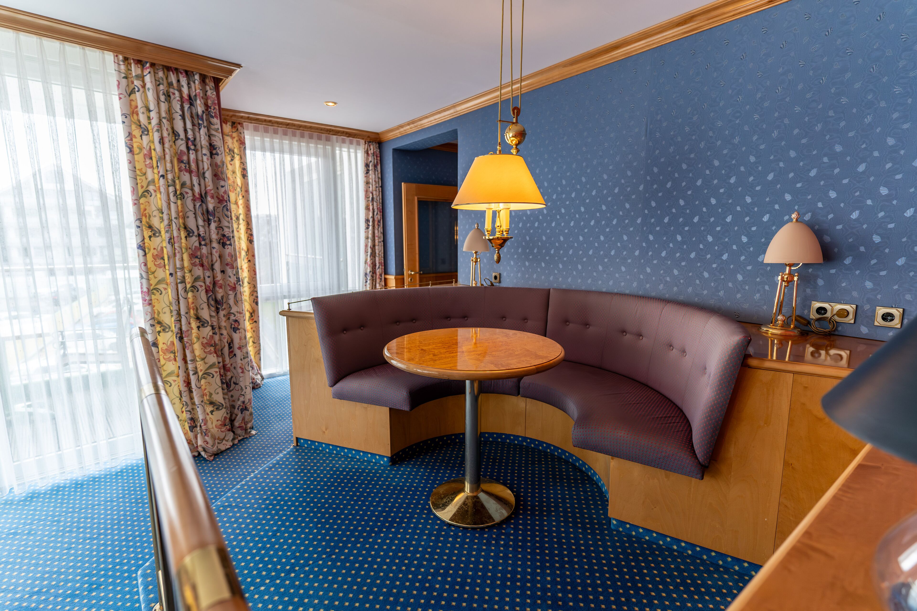 Una habitación con un sofá curvo, una mesa redonda y una pared azul estampada.