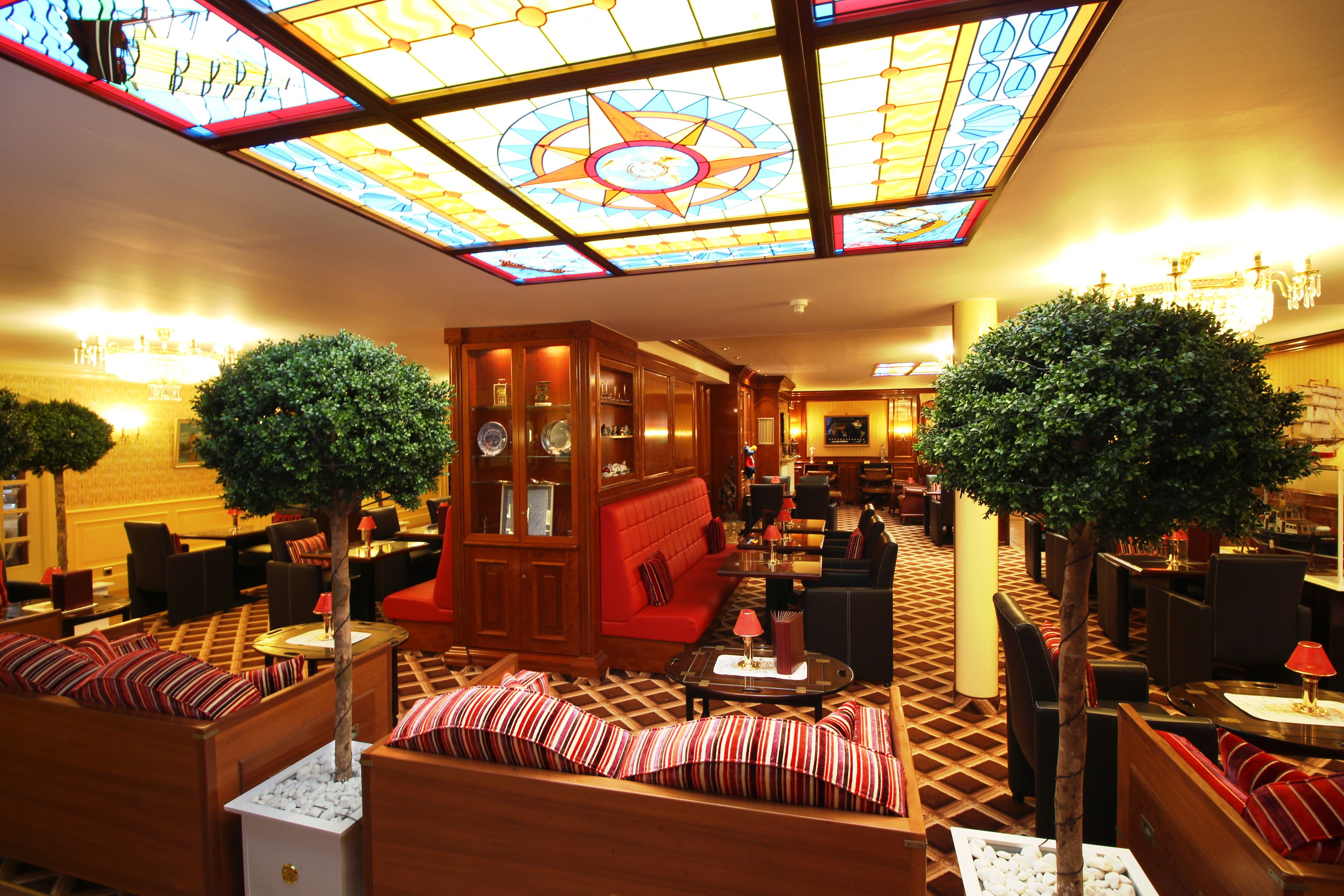A hotel lobby with a central seating area, wooden furniture, and a large stained glass ceiling.