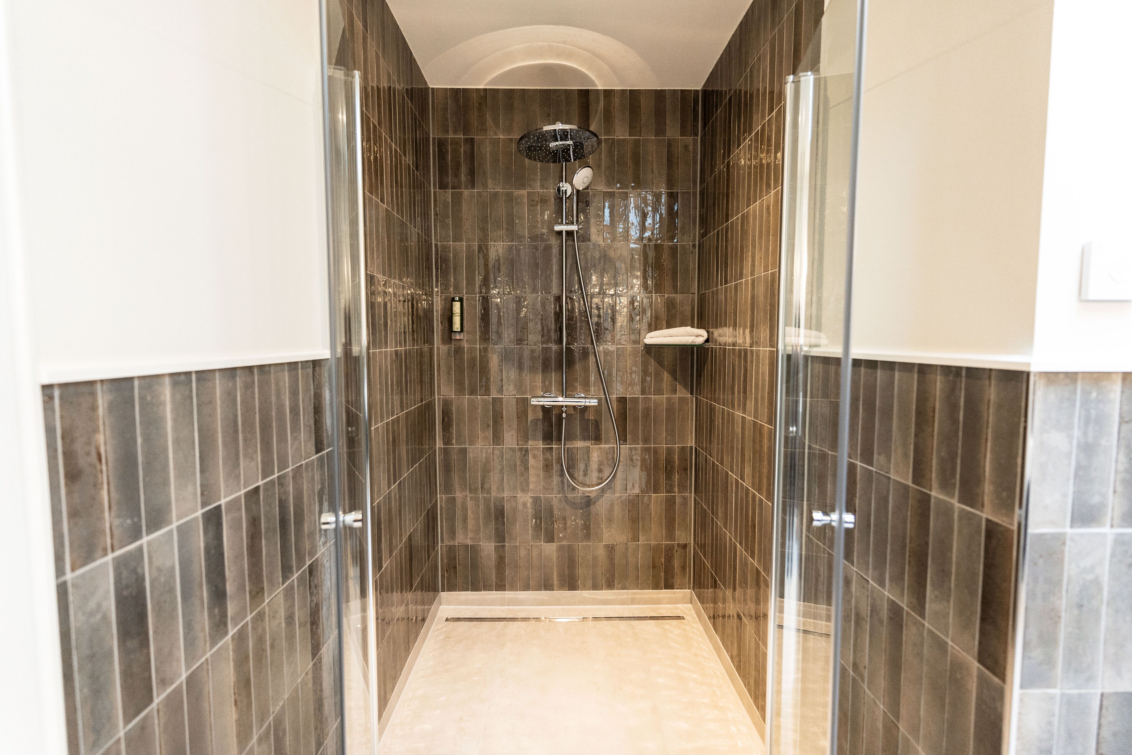 A walk-in shower with a glass door, tiled walls, and a handheld showerhead.