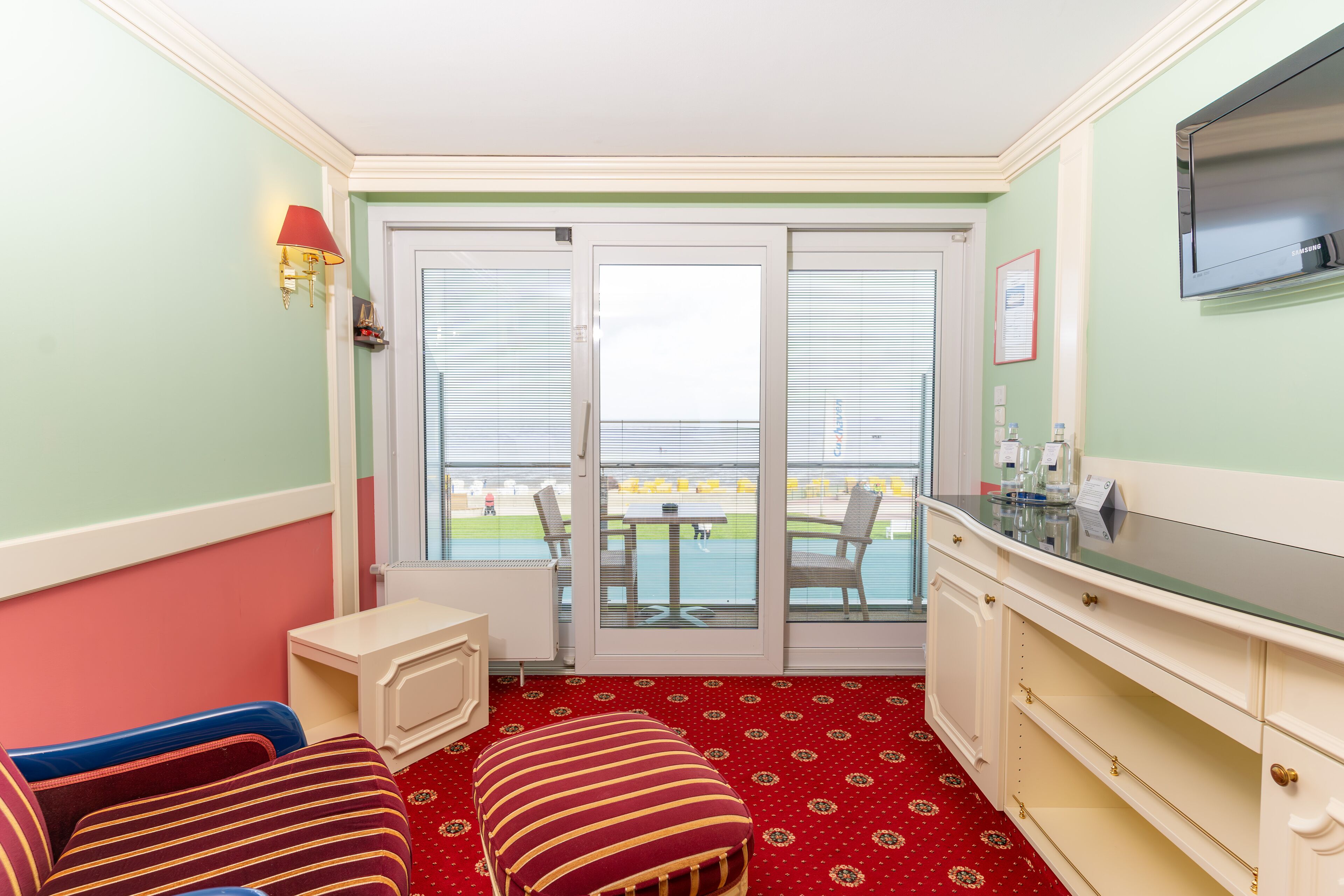 A room with a red carpet, a white cabinet, a television, and a sliding glass door leading to an outdoor area.