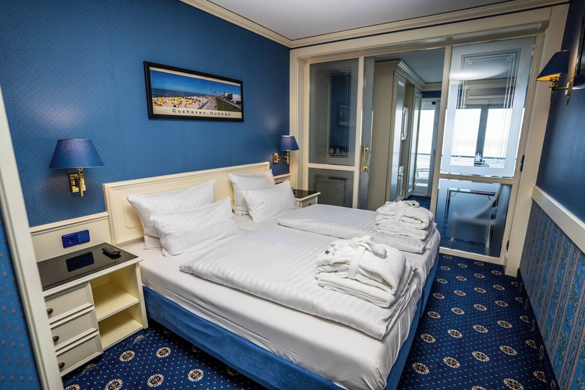 Habitación de hotel con una cama grande, dos mesitas de noche, un tocador, un espejo y una puerta que da a un baño.