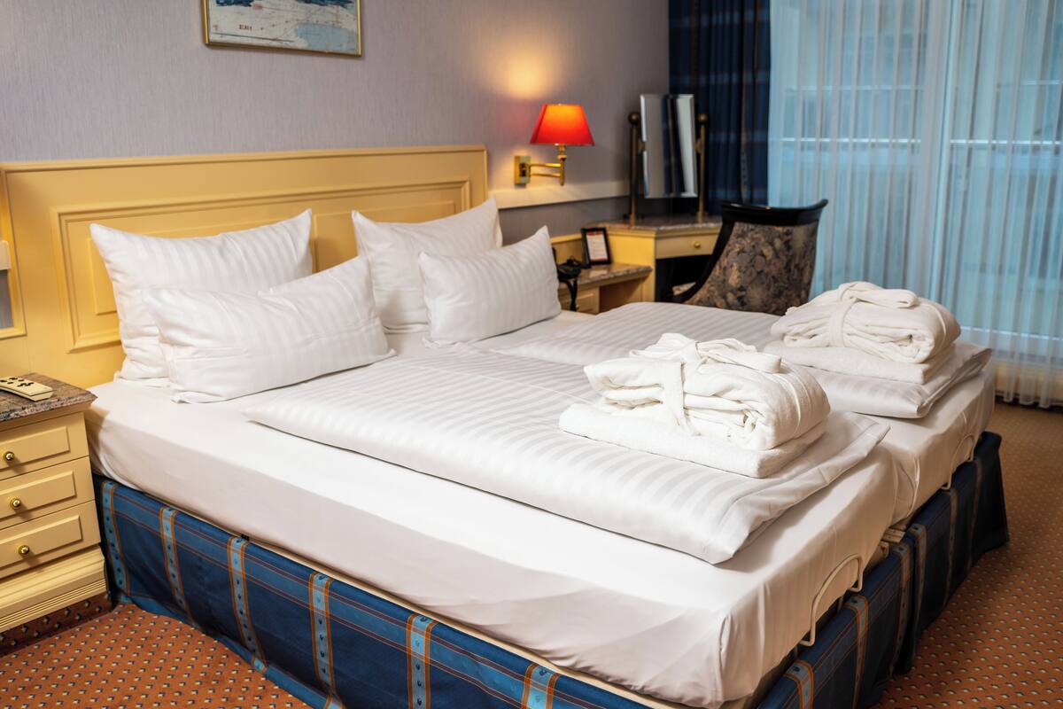 Habitación de hotel con una cama bien hecha, un escritorio con lámpara, una silla y un televisor.