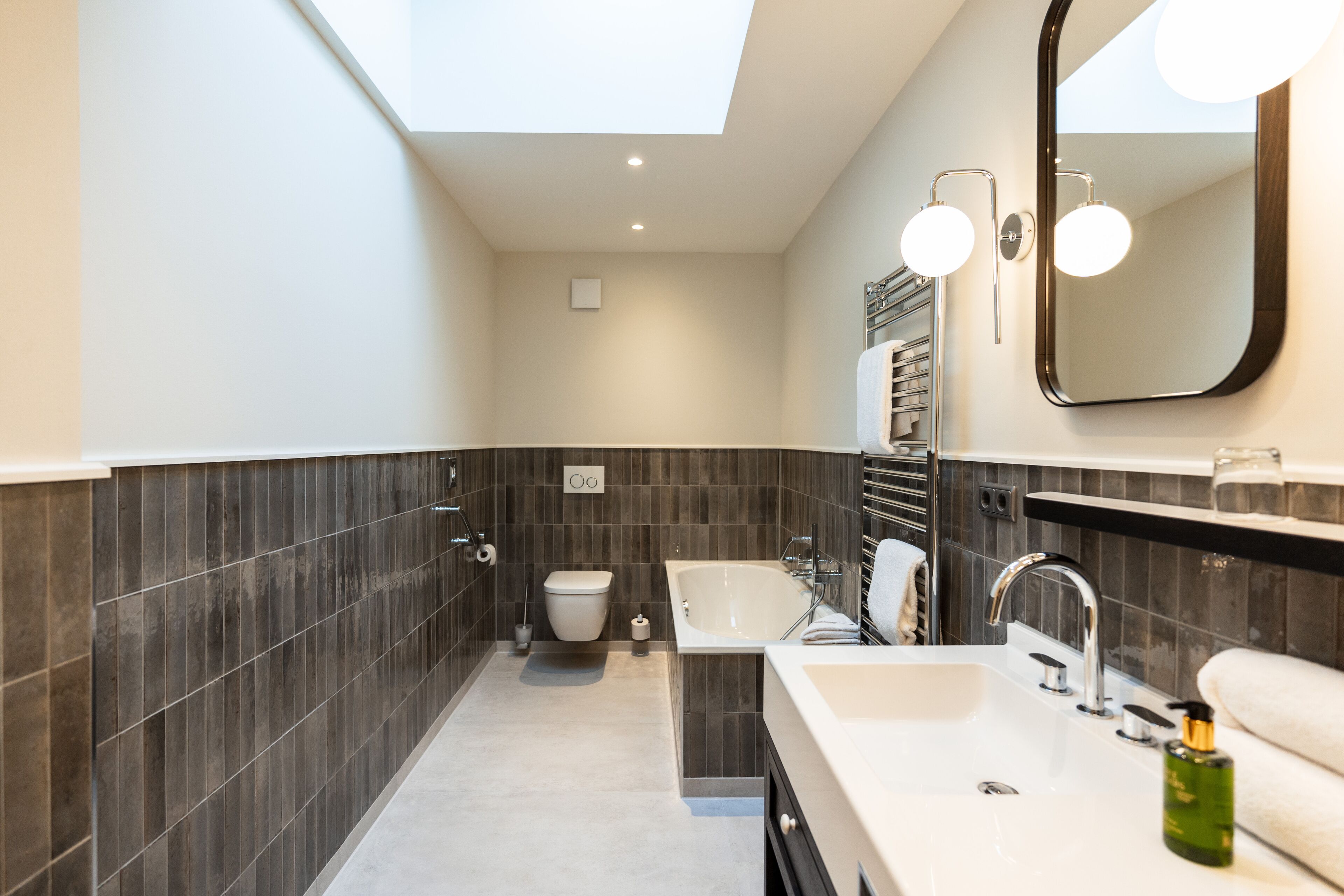 Une salle de bain moderne avec un puits de lumière, une baignoire, un lavabo et des toilettes.