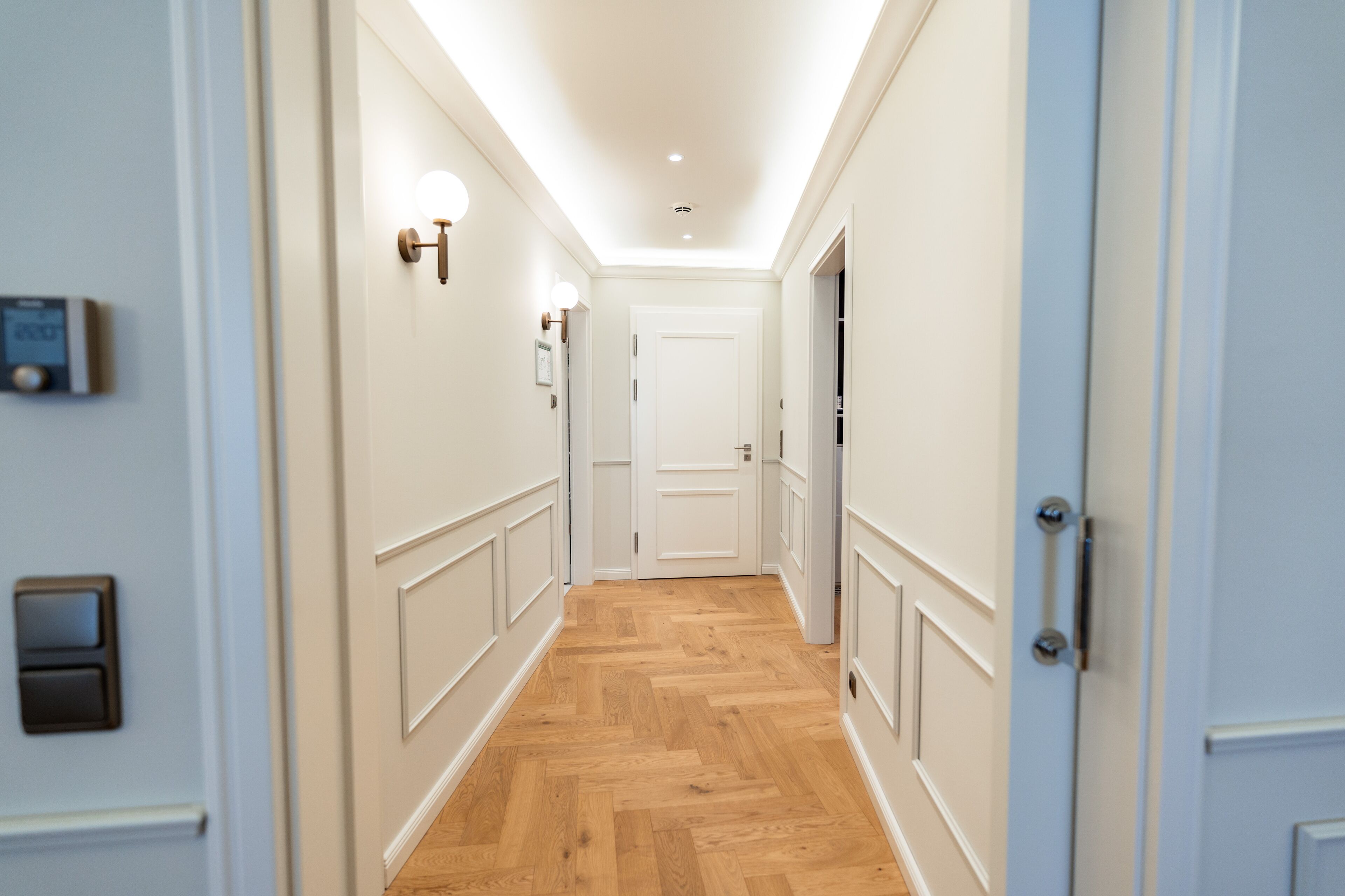 A hallway with wooden flooring, white walls, and a white door at the end.