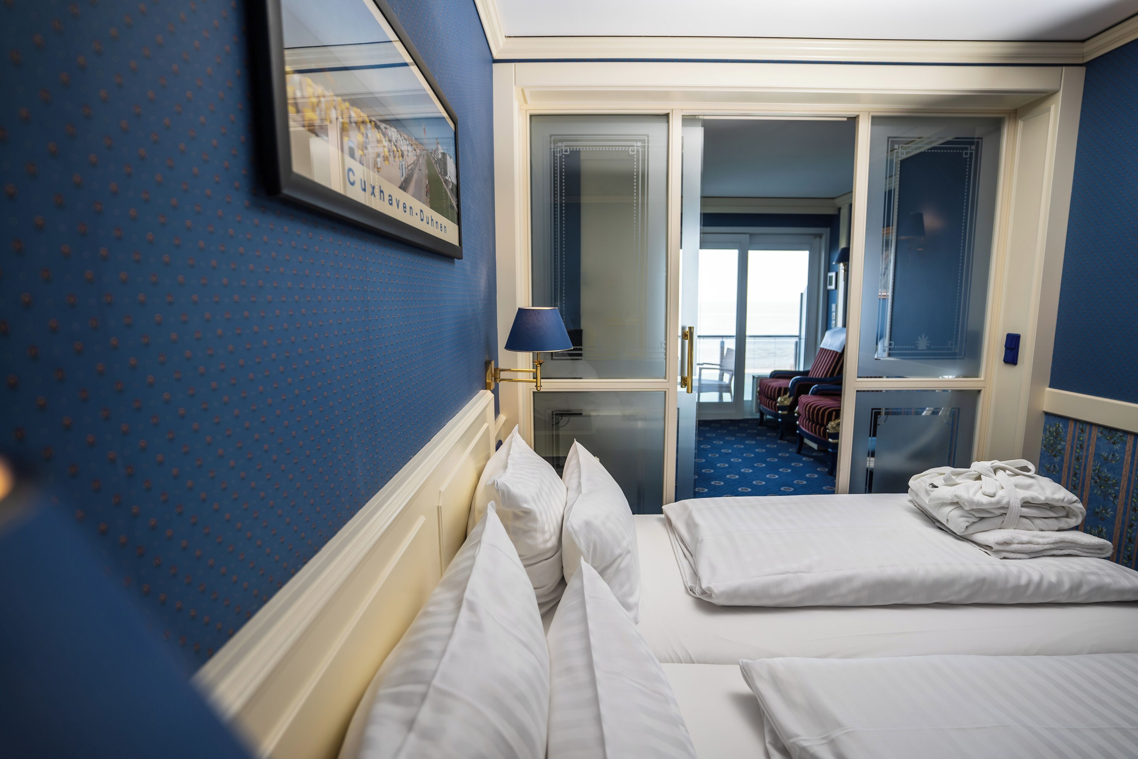 Hotellihuone, jossa on sänky, sininen seinä, kehystetty taulu ja ikkuna.