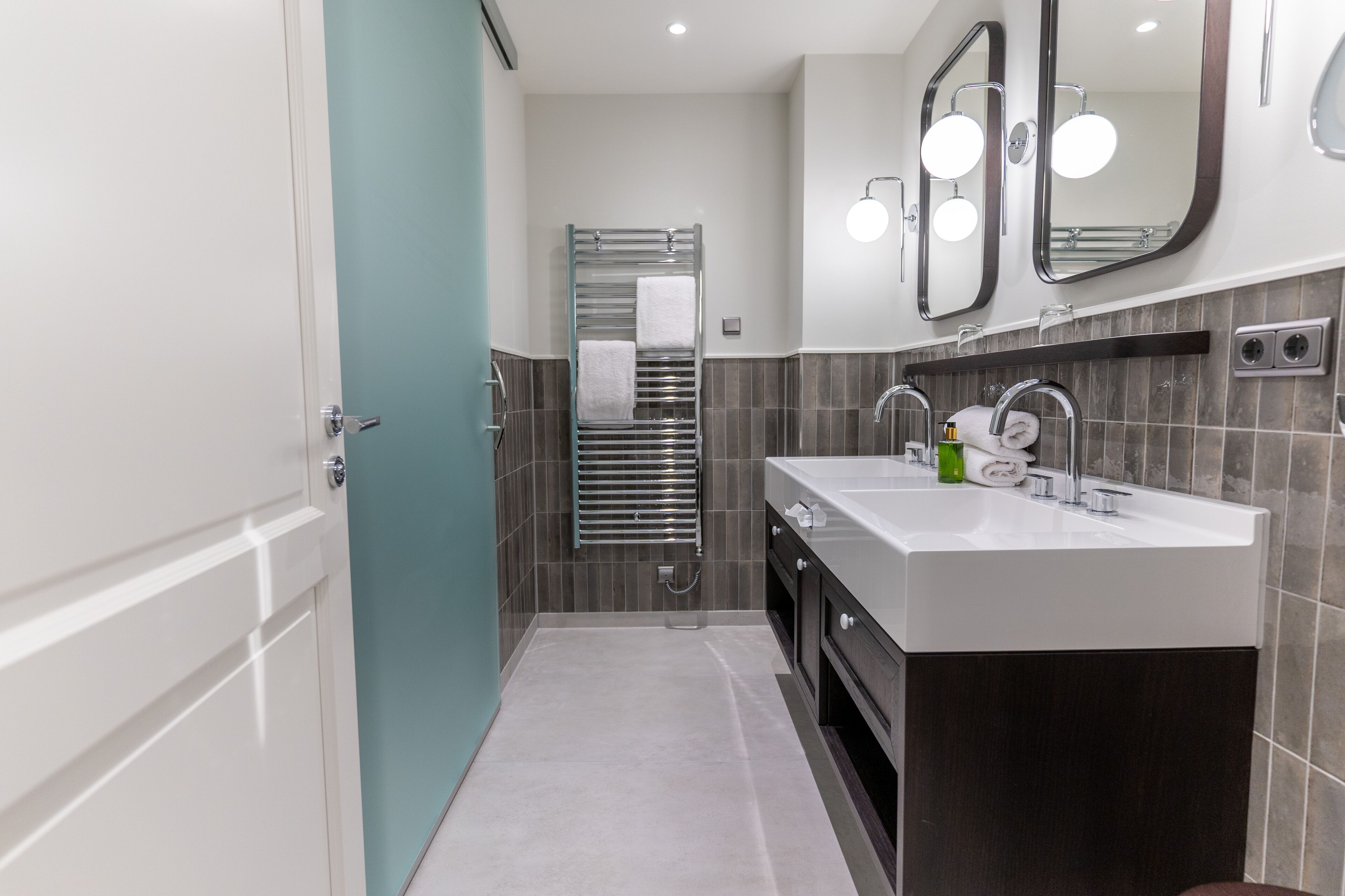 A modern bathroom with a double sink, a glass shower enclosure, and a large mirror above the sink.