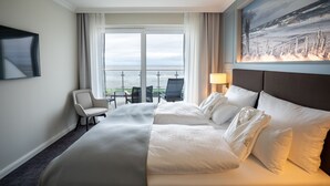 A hotel room with a large bed, a desk, and a chair. There is a window with a view of the sea. - Hotel Strandperle (Cuxhaven)