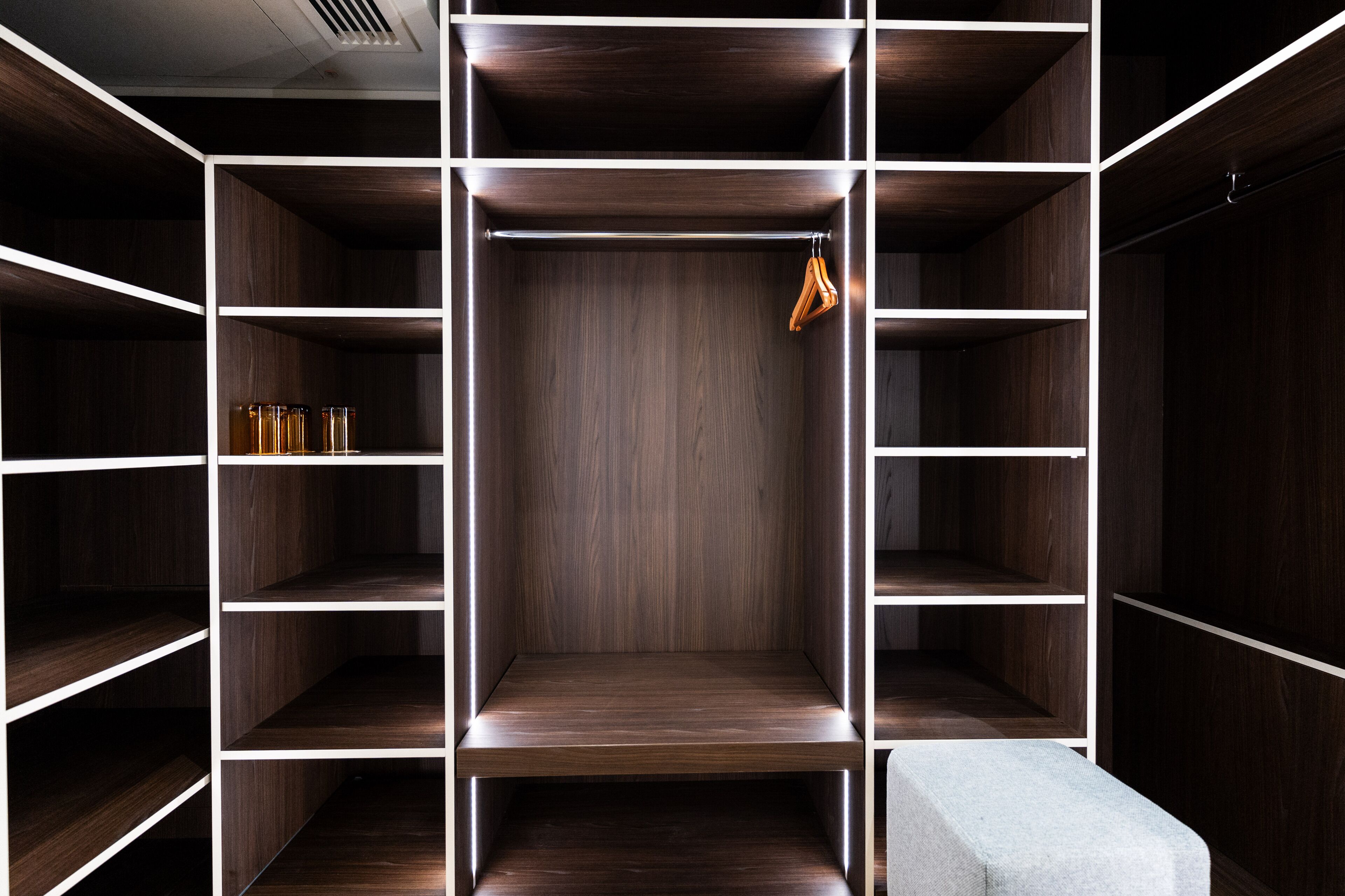 A modern walk-in closet with multiple shelves and hanging space, featuring a central wooden panel and a hanging rack.