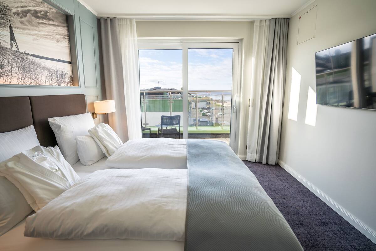 Habitación de hotel con una cama grande, un escritorio, una silla, un televisor y un balcón con vistas a la ciudad.