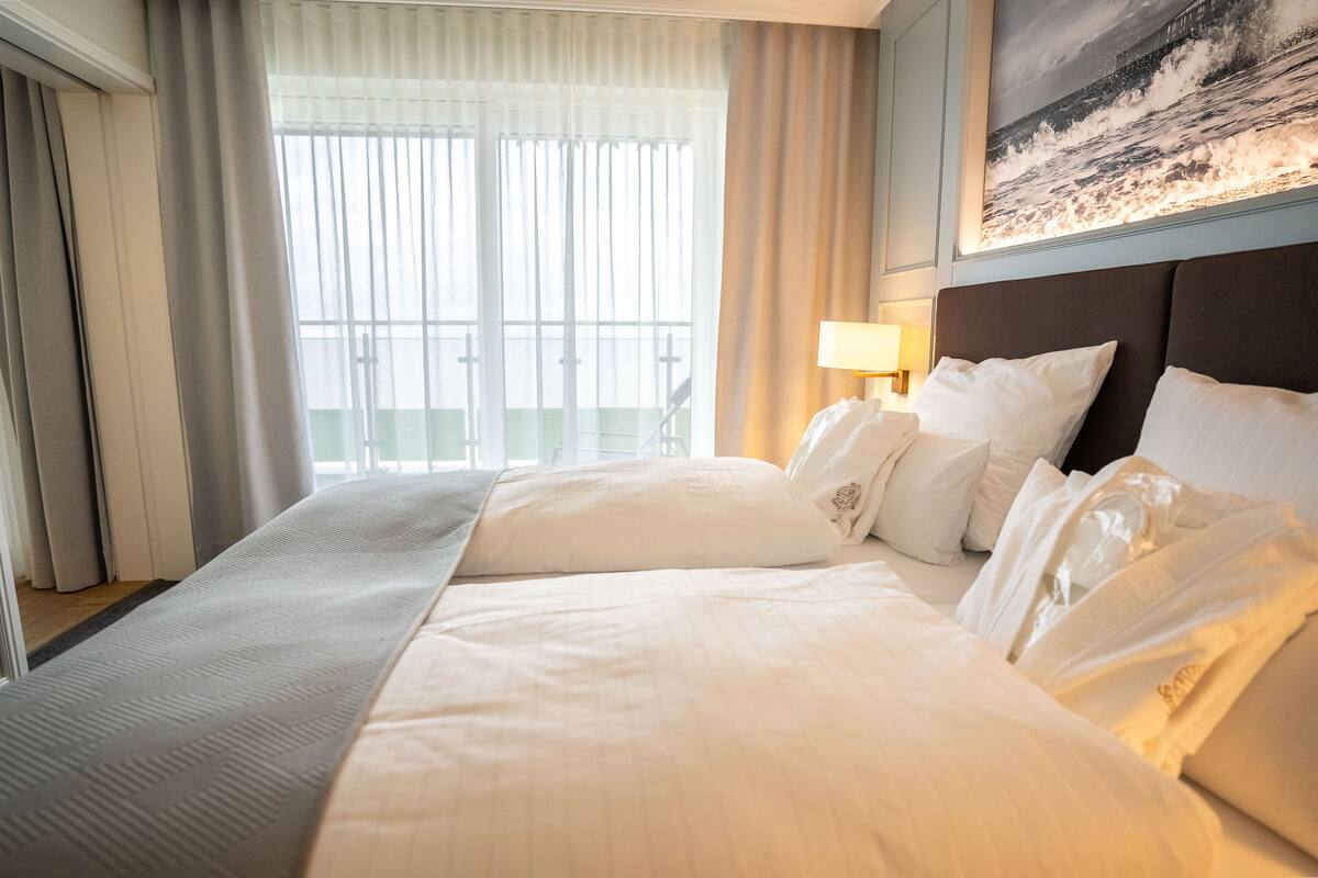 Habitación de hotel con una cama grande, una mesita de noche con lámpara y vista al mar por la ventana.