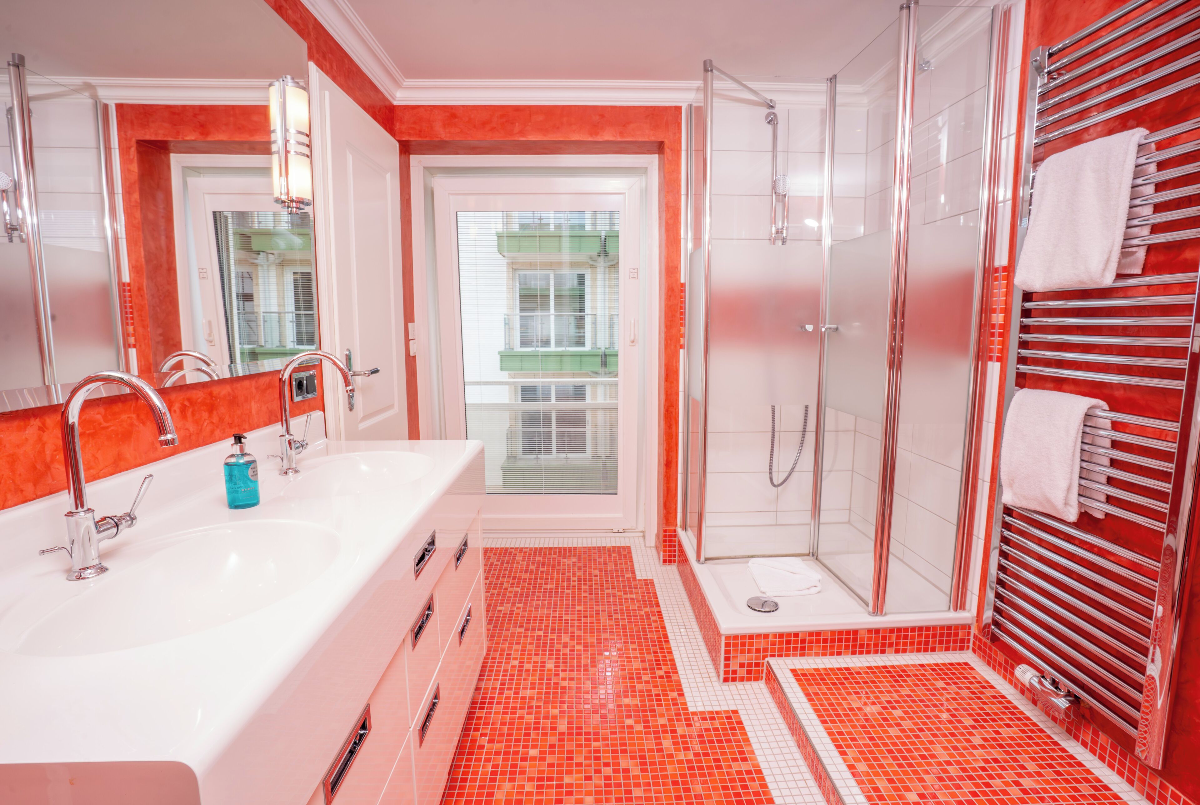 Un bany modern amb un lavabo gran de color blanc, un compartiment de dutxa de vidre i un paviment de rajoles vermelles.