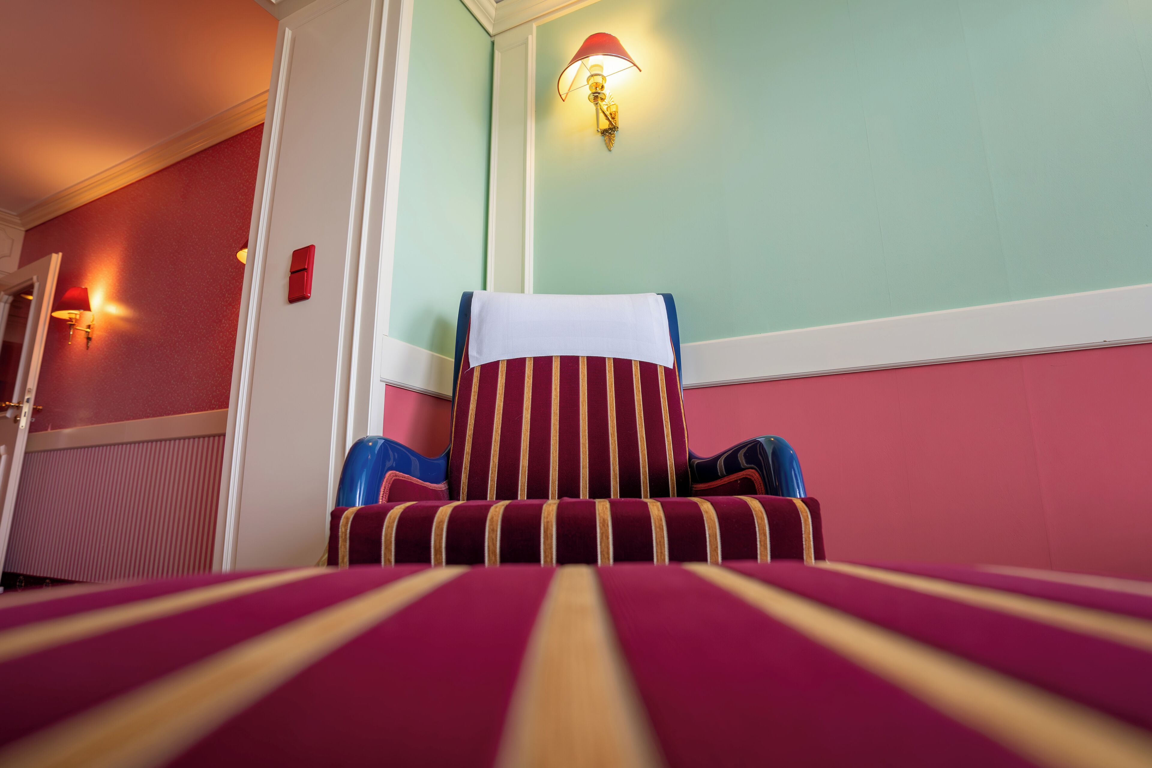 Ein Hotelzimmer mit einem gestreiften Ohrensessel, einer Wandleuchte und einer Heizung.
