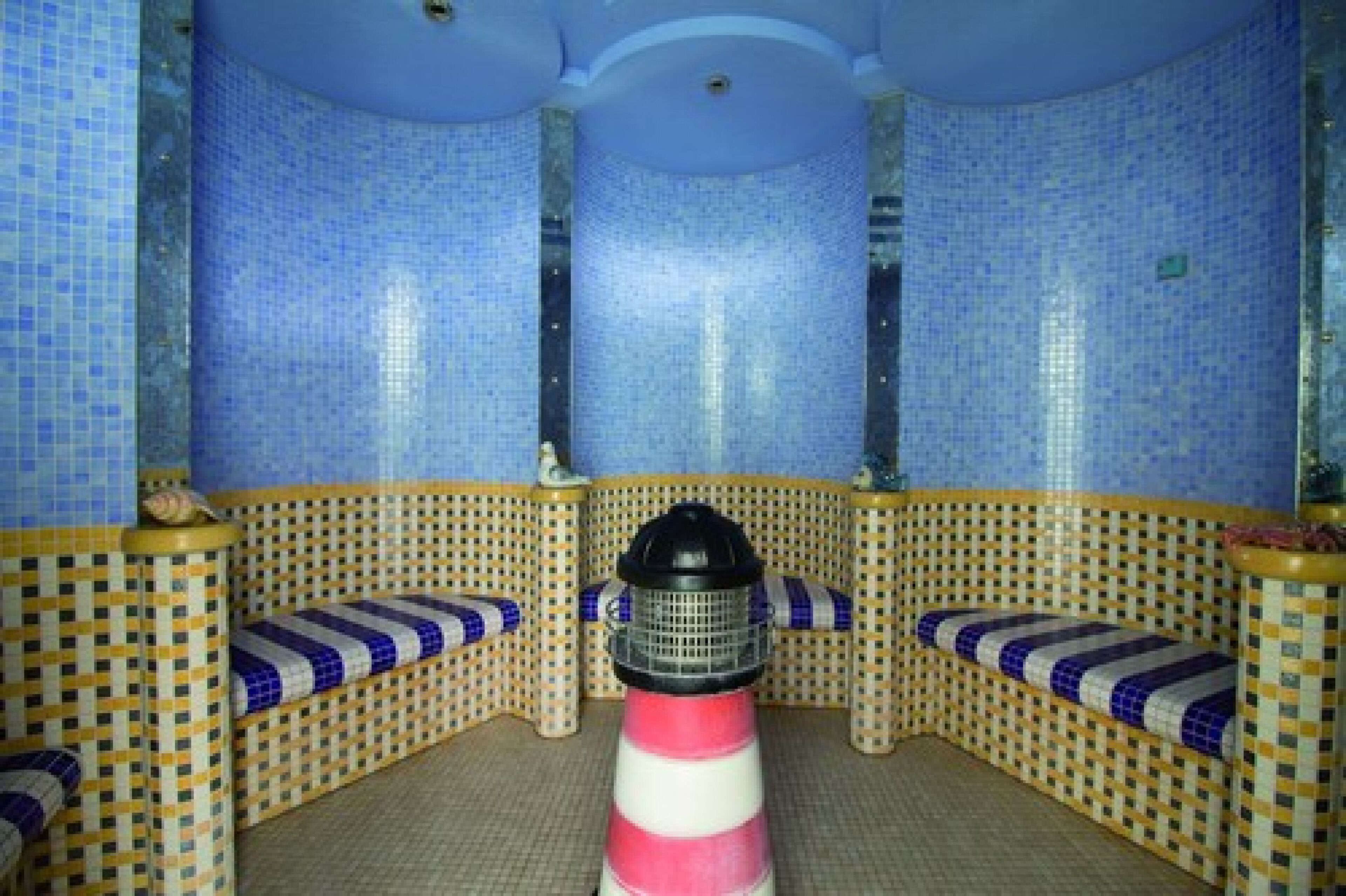 A spa room with blue mosaic walls, a central massage chair, and a small table with a lamp.
