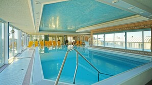 A large indoor swimming pool with clear blue water, surrounded by yellow chairs and a tiled floor. - Hotel Strandperle (Cuxhaven)