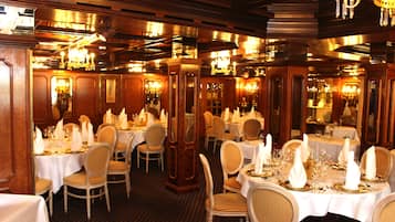 Un comedor formal con varias mesas dispuestas para el servicio, paneles de madera en las paredes y candelabros.