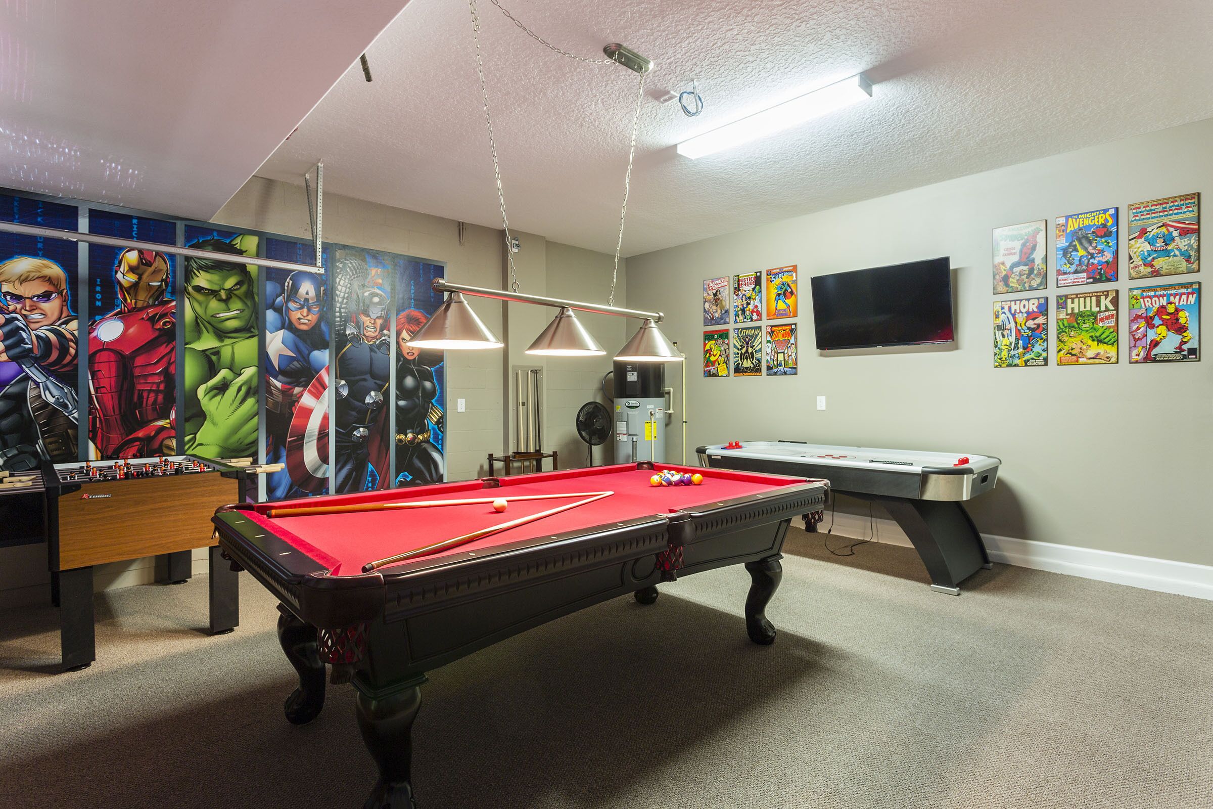 Ein Billardtisch mit roter Spielbahn, ein Kicker und ein an der Wand befestigter Fernseher.