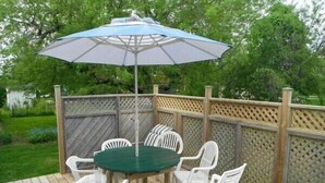 A covered outdoor patio with a round table and white chairs, surrounded by a wooden deck and a lattice fence.