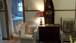 A cozy room with a bed, a chair, a small table with decorative items, and a bookshelf.