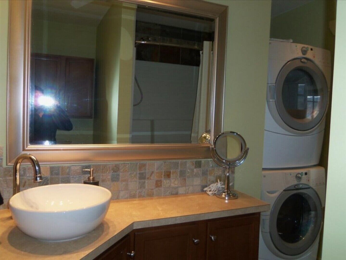 A bathroom with a large sink, a mirror, a washing machine, and a tiled backsplash.