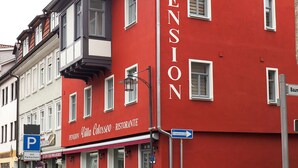 A red building with "PENSION" written on the side, a sign for "Pension mit Colosseo - Ristorante", and a blue parking sign. - Pension Villa Colosseo (Meiningen)