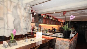 A bar area with a stone counter, shelves of bottles, and a decorative flower arrangement. - Pension Villa Colosseo (Meiningen)