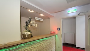 A reception area with a stone wall, a reception desk, a sign indicating the reception, a red carpet leading to a door, and a white radiator. - Pension Villa Colosseo (Meiningen)