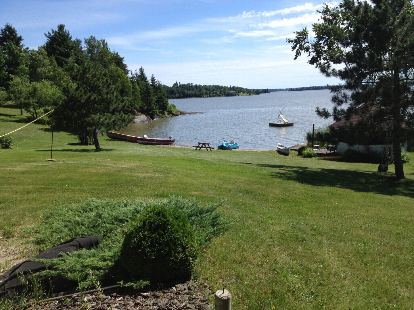 A lakeside property with a grassy lawn, a picnic table, and boats.