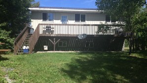 A two-story house with a wooden deck, a satellite dish, and a small outdoor seating area. - Elm Bay Cabin Rentals - Cottage #1 (Dryden)