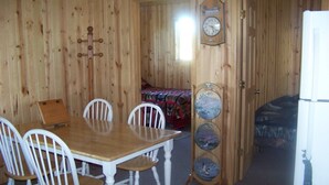 A wooden interior with a dining table and chairs, a clock, and a bed with a patterned blanket. - Elm Bay Cabin Rentals - Cottage #1 (Dryden)
