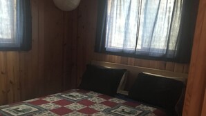 A wooden room with a bed, two windows with curtains, and a round light fixture. - Elm Bay Cabin Rentals - Cottage #1 (Dryden)