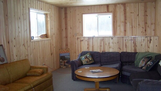 A cozy room with wooden walls, a brown sofa, a gray sectional sofa, and a round coffee table. - Elm Bay Cabin Rentals - Cottage #1 (Dryden)