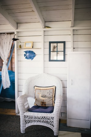 A white wicker chair with a cushion, a fish decoration, a framed picture, and a white cabinet.